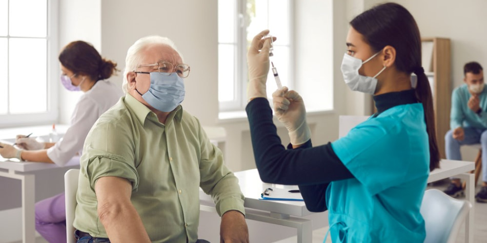 A nurse fills a needle to give an older man a vaccine.