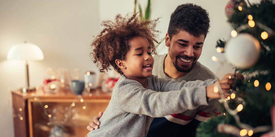 A child decorates a Christmas tree with their dad.