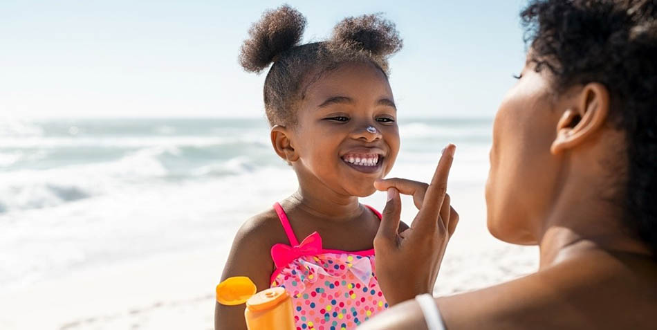 A mother applies sunscreen on her daughter's nose.