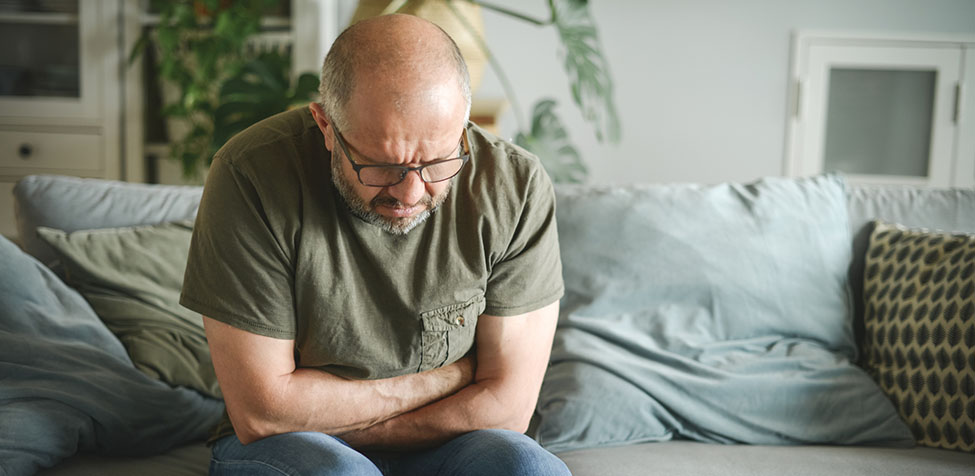 Man sitting on a couch bending forward clutching his stomach.